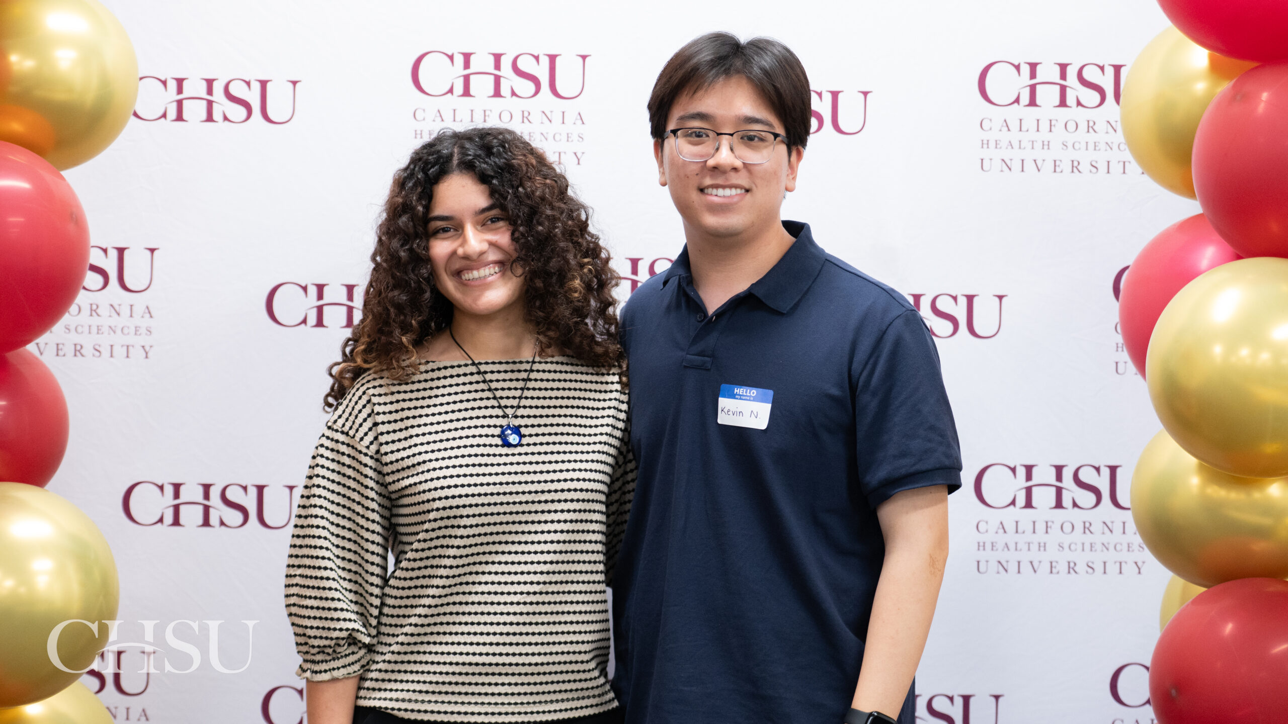 Two incoming CHSU MSBS students pose together in front of a California Health Sciences University backdrop during orientation.