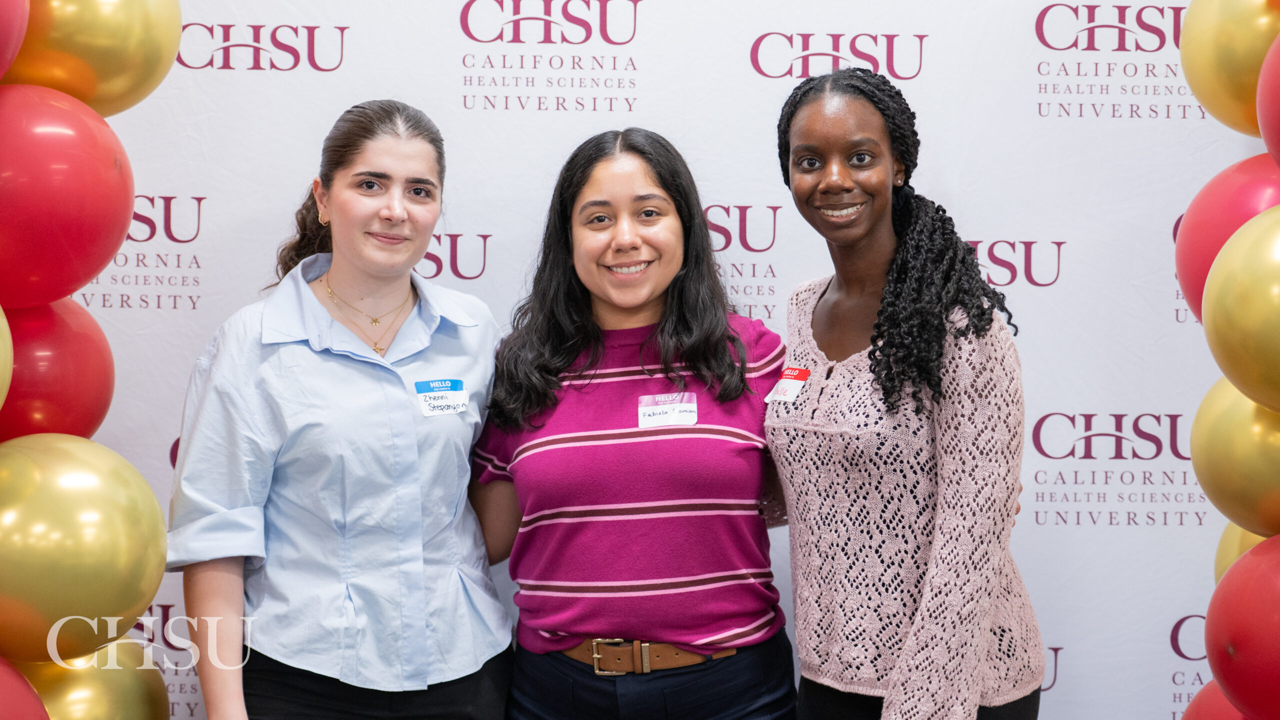 Three incoming CHSU MSBS students pose in front of a California Health Sciences University backdrop framed by red and gold balloons.