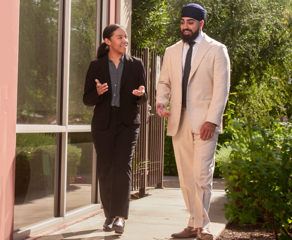 2 people walking by building and trees
